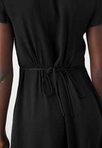 Black dress with a relaxed fit, cinched at the waist with a matching tie. Smooth texture with short sleeves and a flowing design.