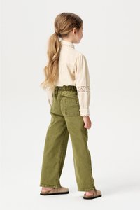 Hellbeige Bluse mit Spitzenakzenten an den Ärmeln, kombiniert mit olivgrünen weit geschnittenen Hosen, ausgestattet mit einem elastischen Bund und Gesäßtaschen.