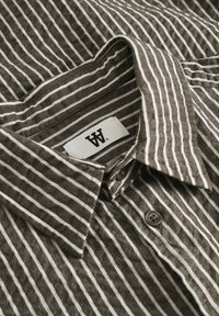 Brown and white striped button-up shirt with a collar, featuring a woven texture and two brown buttons near the neck. Brand label visible.