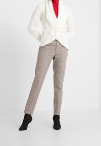 Cárdigan blanco con canalé y cuello de chal, complementado con pantalones a cuadros en rojo, negro y beige. Botines de tacón alto negros.