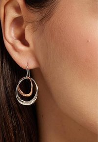 Pendientes circulares de plata y oro rosa, con anillos anidados. Textura suave con un acabado pulido y un diseño de gancho colgante delgado.