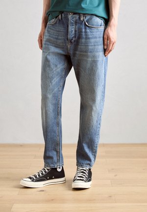 Lys blå denimjeans med avslappet passform, med fem lommer, knappesteg og subtile viskingdetaljer. Sammen med svarte joggesko.