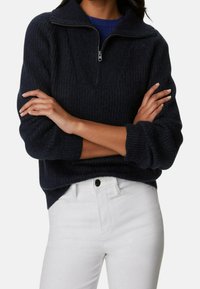 Marineblauw gebreid trui met een kwart rits, geribbeld textuur en een ontspannen pasvorm. Gecombineerd met witte jeans voor contrast.