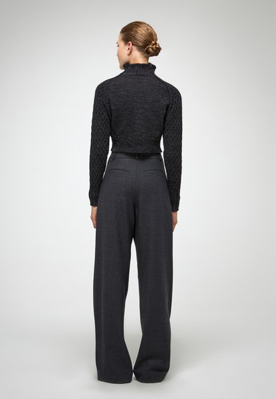 Korte zwarte gebreide trui met een textuurpatroon, hoge kraag; gecombineerd met hoogzitende donkergrijze wijde broek, met een gladde stofafwerking.