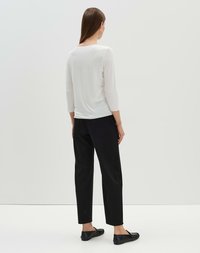 Haut blanc à manches longues avec encolure dégagée, pantalon noir ajusté et chaussures à enfiler noires, vues de dos sur un fond clair.