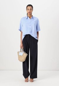Light blue short-sleeve shirt, dark wide-leg trousers, and a woven handbag. Smooth fabric with buttons; bag features a handle and a flat tag.