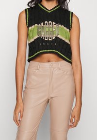 Černý pletený crop top s zelenými a béžovými pruhy, s nápisem "RAGGED JEANS" výrazně zobrazeným vepředu.