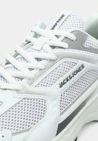Baskets en mesh blanches avec des accents gris, dotées d'un col rembourré, d'un système de laçage et d'un logo "JACK & JONES" sur le côté.