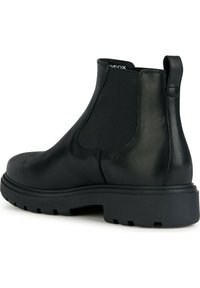 Stivaletto in pelle nera con pannelli laterali elastici, punta rotonda e una robusta suola in gomma con un motivo di grip testurizzato.