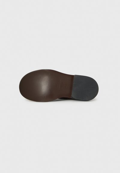 Suela de zapato de cuero marrón con forma redondeada, que presenta una superficie lisa, una pequeña impresión de logo y una tapa de tacón negra contrastante.