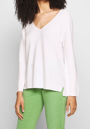 Maglione rosa chiaro lavorato a maglia con scollatura a V e maniche lunghe. Presenta spacchi laterali all'orlo e un tessuto texture, abbinato a pantaloni verdi.