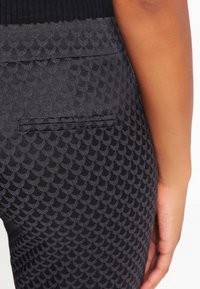 Pantalon texturé noir avec un motif répétitif en forme d'écailles de poisson, détail de poche arrière et finition en tissu lisse.