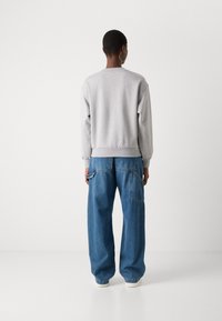 Felpa grigia con polsini e orlo a costine abbinata a pantaloni in denim blu dalle linee morbide, con tasche laterali e una silhouette rilassata.