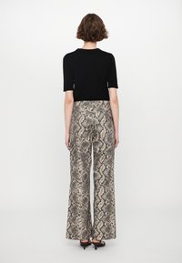 Top nero aderente con maniche corte abbinato a pantaloni a gamba larga a vita alta con motivo a serpente beige e nero.