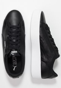 Sneakers in pelle nera con finitura testurizzata, suola in gomma bianca, lacci piatti e un'evidente branding Puma sui lati e sulla linguetta.