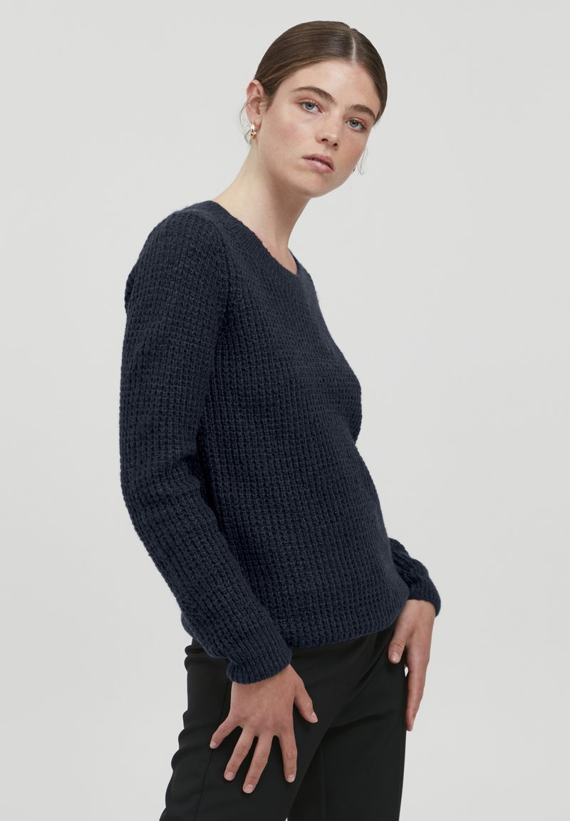 Marineblauer Strickpullover mit strukturiertem Muster, Rundhalsausschnitt und langen Ärmeln, kombiniert mit schwarzen Hosen.