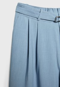 Lichtblauwe geplooide broek met een stoffen textuur, voorzien van een brede tailleband en een riem met een zilveren gesp.