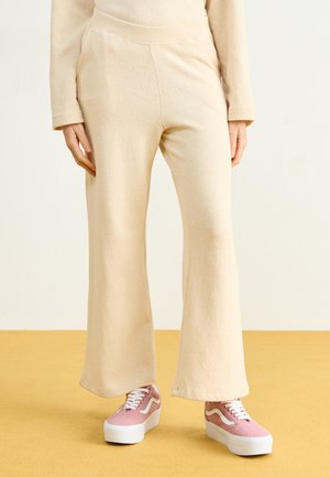 Beige flared pants made of soft fabric with a smooth texture and an elastic waistband, paired with pink platform sneakers.