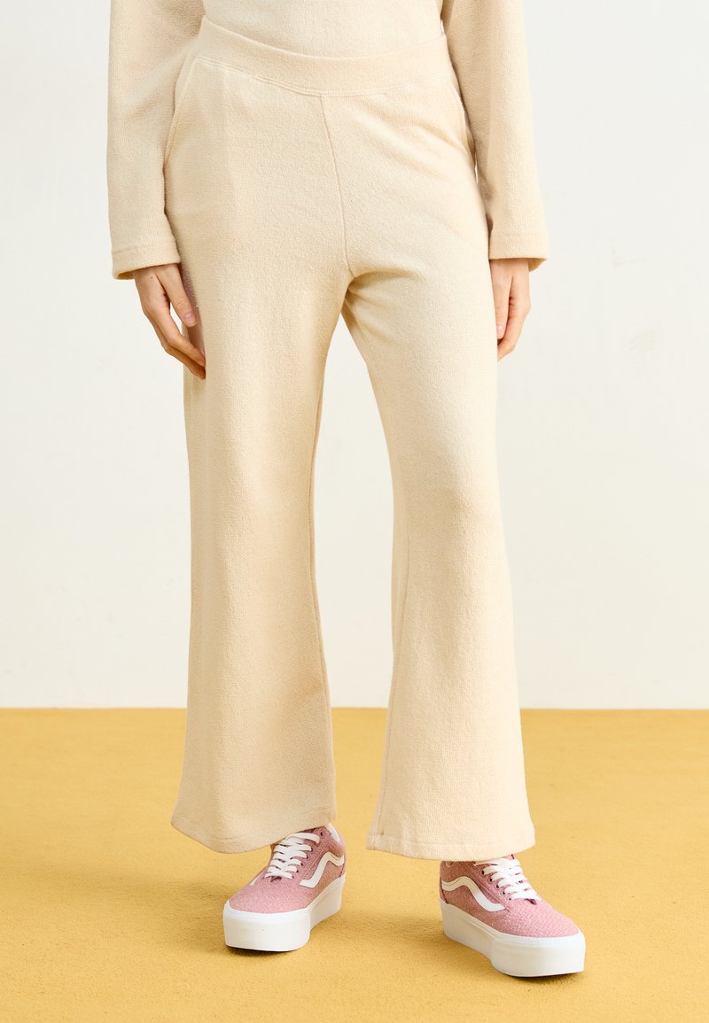 Beige utsvingte bukser laget av mykt stoff med en jevn tekstur og elastisk liv, paret med rosa platå-sneakers.