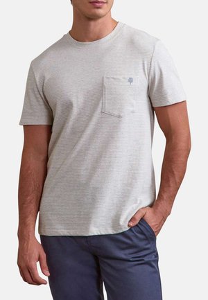 Homme portant un t-shirt à manches courtes rayé gris clair avec une poche poitrine et un pantalon bleu foncé, une main dans la poche.