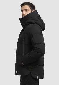 Jachetă puf cu un guler înalt, buzunar lateral cu fermoar și detaliu cu cataramă ajustabilă la talie. Material neted cu textură căptușită.