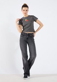 Grå ribbet crop-top med kirsebæroverføring, kombinert med høy midje svarte flagrende jeans og svarte sneakers, mot en ensfarget bakgrunn.