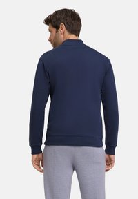 Felpa blu navy con colletto polo e maniche lunghe, realizzata in un tessuto morbido. I polsini e l'orlo presentano una texture a coste per una vestibilità aderente.