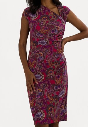 Kobieta ubrana w dopasowaną sukienkę z krótkim rękawem sięgającą kolan, z czerwono-fioletowo-pomarańczowym wzorem paisley i marszczeniami po boku.