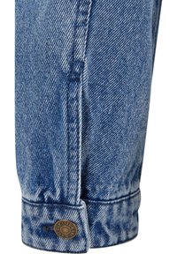 Jeans de mezclilla azul claro con dobladillo vuelto, con costuras en contraste y un detalle de botón en bronce. Tela texturizada con un tejido clásico.