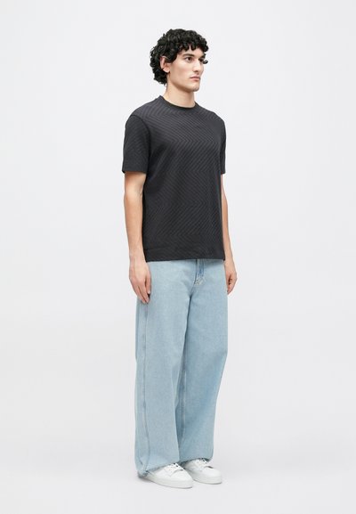 Čierne tričko s krátkym rukávom s textúrovaným cikcak vzorom, v kombinácii so svetlomodrými džínsami s širokými nohavicami a bielymi teniskami.