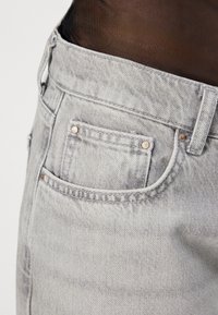 Gray denim jeans feature a slim fit, five-pocket design with a front pocket stitched with copper rivets and a textured fabric finish.