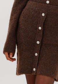 Bruine gestructureerde rok van zacht gebreid materiaal, met decoratieve zilveren knopen aan de voorkant en een split aan de zijkant.