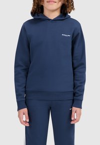 Navyblauwe hoodie van zacht materiaal, met een kangoeroe zak en ribgebreide manchetten. Klein wit logo op de borst. Gecombineerd met bijpassende broek.