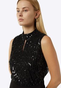 Schwarzes ärmelloses Top mit Pailletten, das über einen hohen Halsausschnitt und ein Schlitzdetail verfügt. Glatte Textur mit einer taillierten Silhouette.