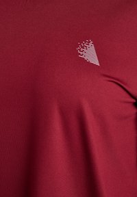 Dunkelrotes Sportshirt mit strukturierter Stoffoberfläche, glattem Finish und einem weißen geometrischen Muster auf der linken Brustseite.