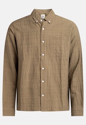 Camisa marrón de manga larga con un patrón de tejido texturizado. Presenta un cuello con botones, bolsillo frontal y botones blancos. Diseño casual.
