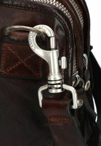 Dettaglio di una borsa in pelle marrone con un fermo in metallo argento e zip, con cuciture visibili e variazioni tattili nella pelle.
