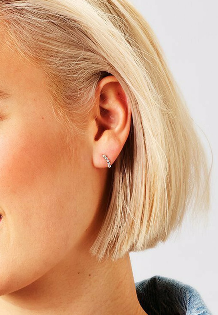Orecchino a cuffia in argento con piccole pietre scintillanti disposte in una linea curva. Presenta un design minimalista adatto a varie occasioni.
