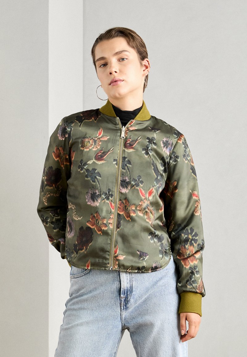 Veste bomber florale verte avec fermeture éclair, présentant une finition satinée, des poignets et un col côtelés, sur un fond gris clair.