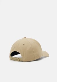 Beige baseballcap med flat skygge, teksturert stoff og justerbar stropp med flere trykknapper bak.