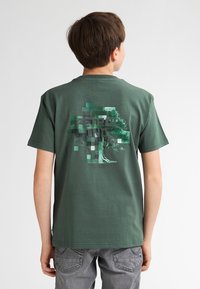 Zelené bavlněné tričko s pixelizovanou grafikou stromu a textem "PETROL" na zadní straně. Krátké rukávy, klasický střih, hladká textura.