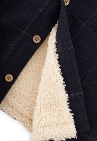 Kofta i ullblandning med en mörkblå utsida, som har en mjuk, krämfärgad fleecefoder och träknappar. Texturerad yta med subtila mönster.