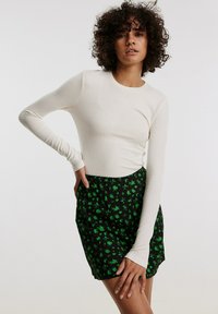 Crème ribbeltrui met lange mouwen, gecombineerd met een zwarte rok met een groen bloemenpatroon. De top heeft aansluitende mouwen en een ronde halslijn.