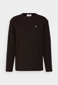 Svart långärmad t-shirt i ribbad bomull, med en liten färgad logotyp på bröstet. Enkel rund halsringning och rak fåll.