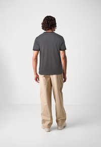 Camiseta de manga corta gris con ribete negro, combinada con pantalones sueltos de color beige. Textura suave, corte estándar, diseño sencillo.