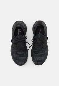 Un par de zapatillas deportivas negras con tejido texturizado, cordones atados y plantillas de marca, fotografiadas desde arriba sobre un fondo blanco.