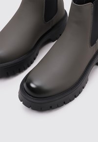 Botines verde oscuro con acabado liso, punta redonda, paneles laterales elásticos y suelas negras de goma resistentes.