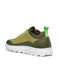 Zapatillas verdes y beige con parte superior de malla, acentos de goma, puntera redonda y suela texturizada, presentando cordones verdes brillantes y etiqueta en el talón.