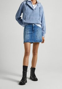 Světle modrá kordurová mikina s kapucí a přední kapsou, kombinovaná s denimovou miniskirtou s knoflíkovým zapínáním a viditelným švem. Černé boty na šněrování.