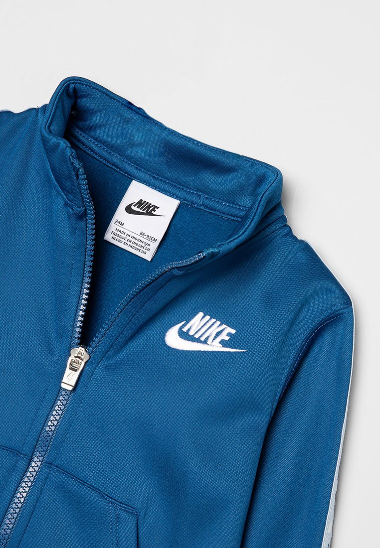 Chaqueta azul de Nike con cremallera, que presenta un cuello alto, logo blanco y una textura de tela suave. Los herrajes en color plata complementan el diseño.